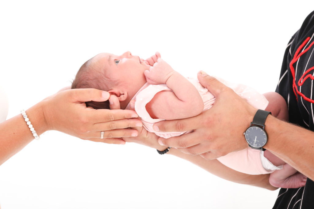 Ein Baby wird von seinen Eltern in den Händen gehalten. Neugeborenenfotografie in Wien