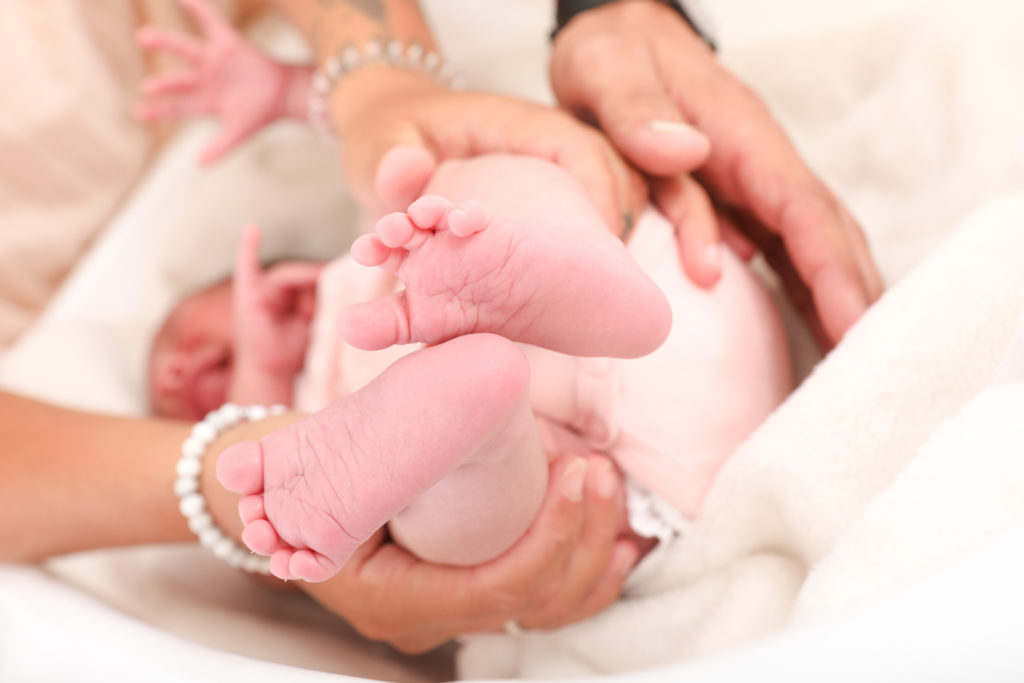 A close-up image of tiny baby feet held in the hands of a parent. Neugeborenenfotografie in Wien
