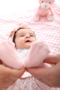 Süße einmonatige rosa Baby im Studio von New Age Fotografie. Das Baby liegt auf einem rosa Hintergrund und trägt ein rosa Kleidchen. Sie hat große, blaue Augen und ein süßes Lächeln