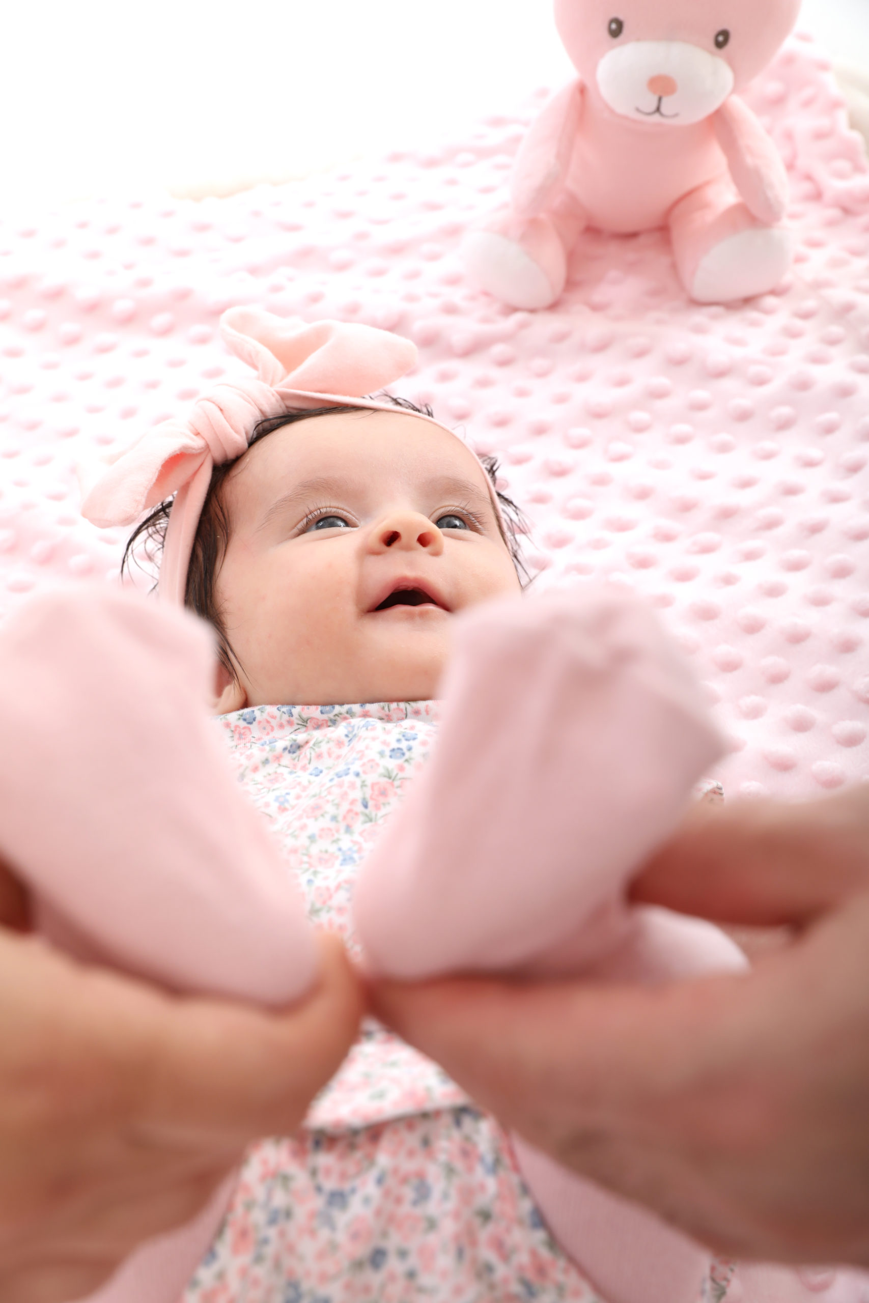 Süße einmonatige rosa Baby im Studio von New Age Fotografie. Das Baby liegt auf einem rosa Hintergrund und trägt ein rosa Kleidchen. Sie hat große, blaue Augen und ein süßes Lächeln
