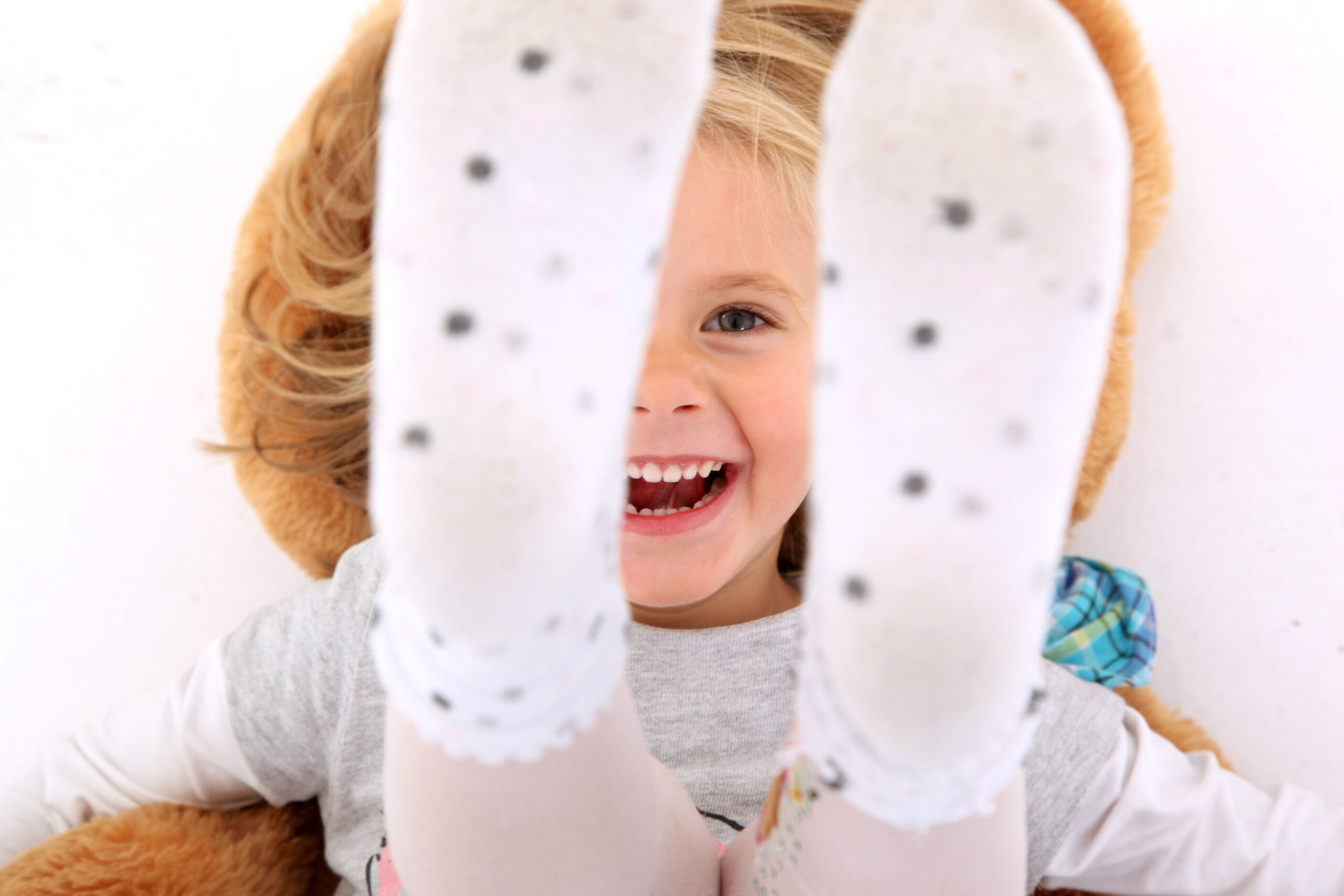 Ein lachendes Kind liegt auf dem Rücken und streckt die in gepunkteten Socken gekleideten Füße in die Kamera.