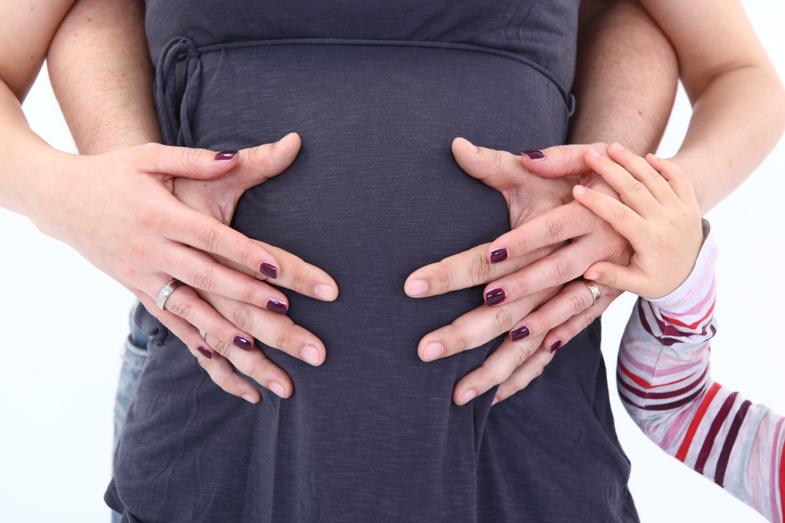 Die Hände einer schwangeren Frau und eines Kindes halten liebevoll ihren Bauch umfasst