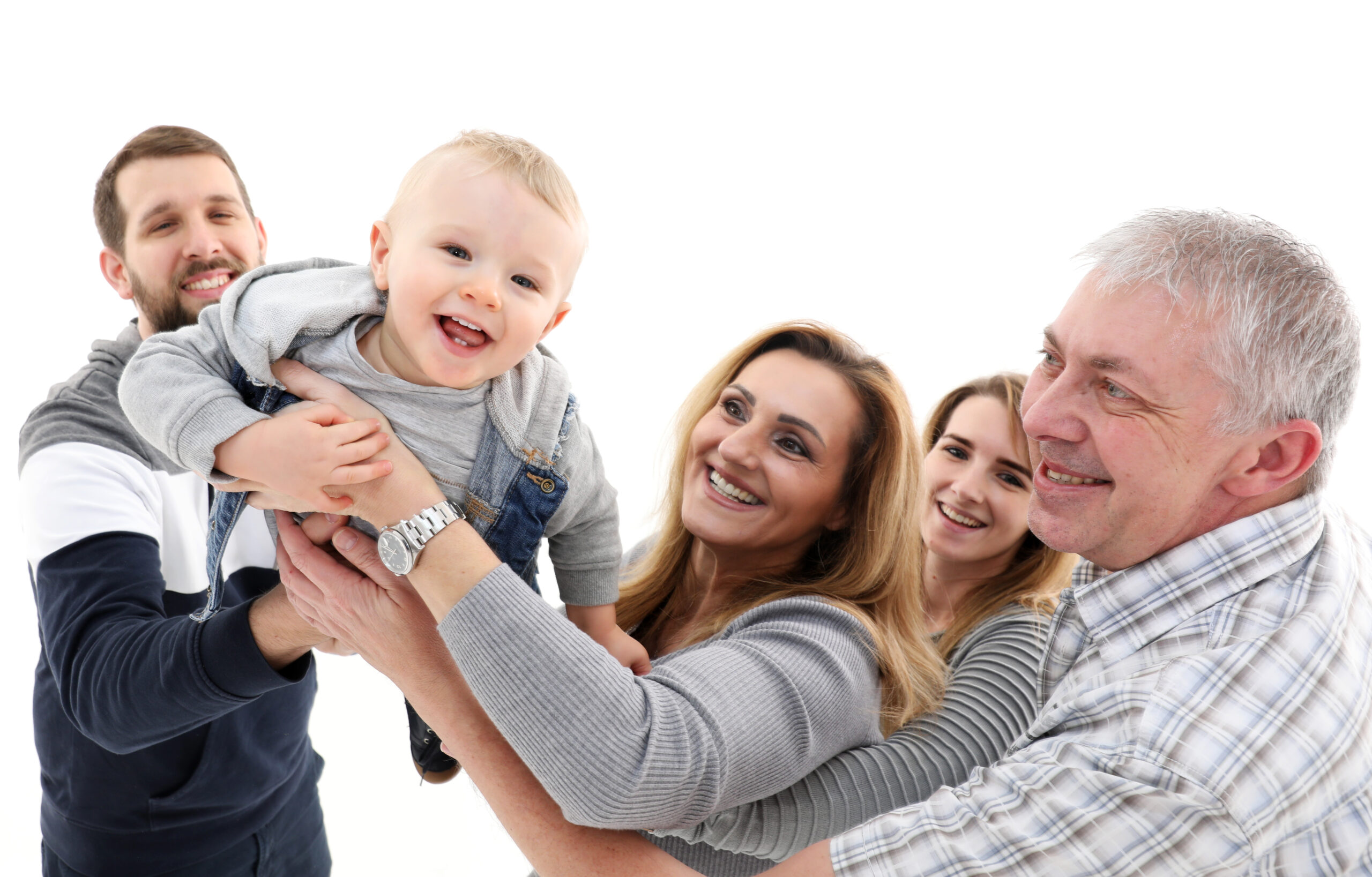 Eine mehrere Generationen umfassende Familie lacht glücklich, während ein Baby hochgehalten wird.