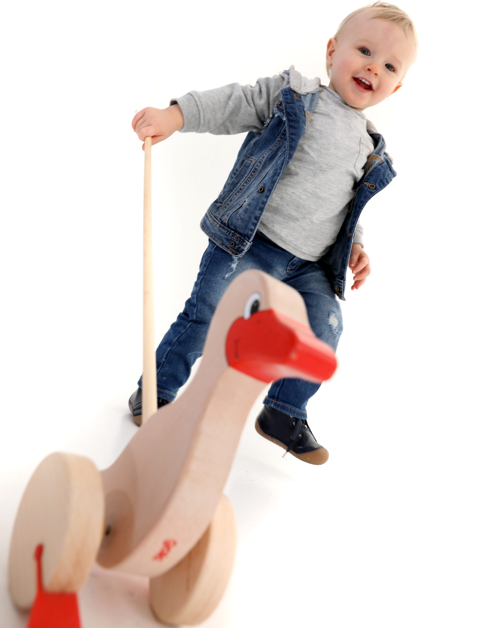 Kleinkind steht neben einem Holz-Schaukelpferd in Form einer Ente auf Rollen.