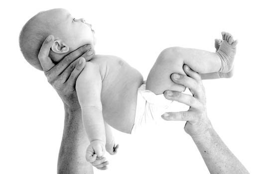 Schwarz-Weiß-Aufnahme eines entspannt aussehenden Babys, das in der Luft gehalten wird.