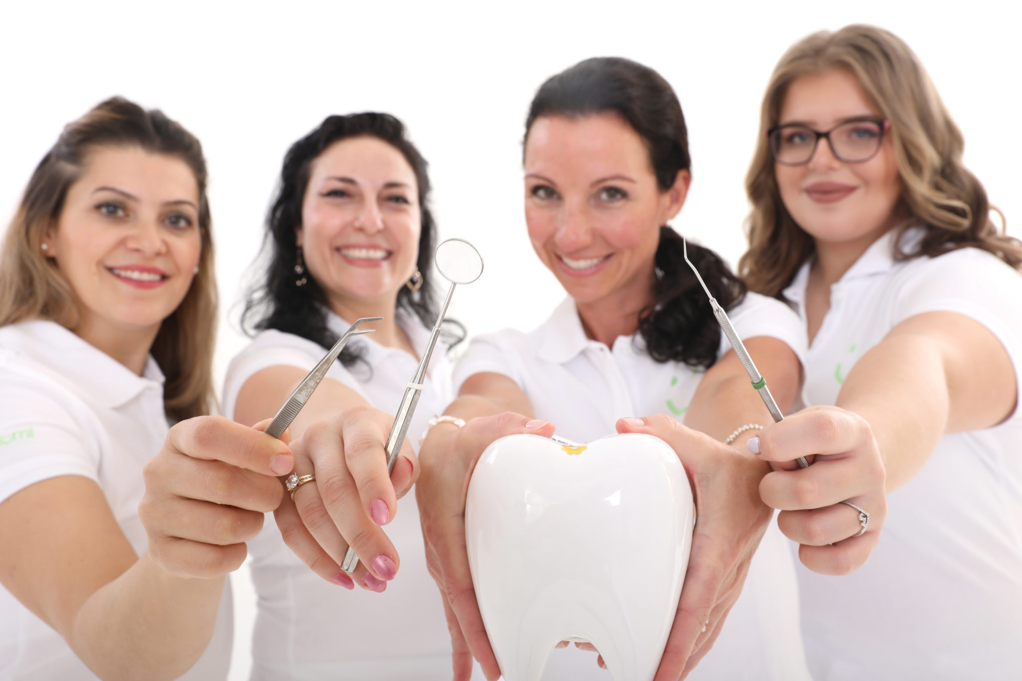 Vier glückliche Frauen im medizinischen Bereich präsentieren zahnärztliche Instrumente und einen großen Modellzahn.