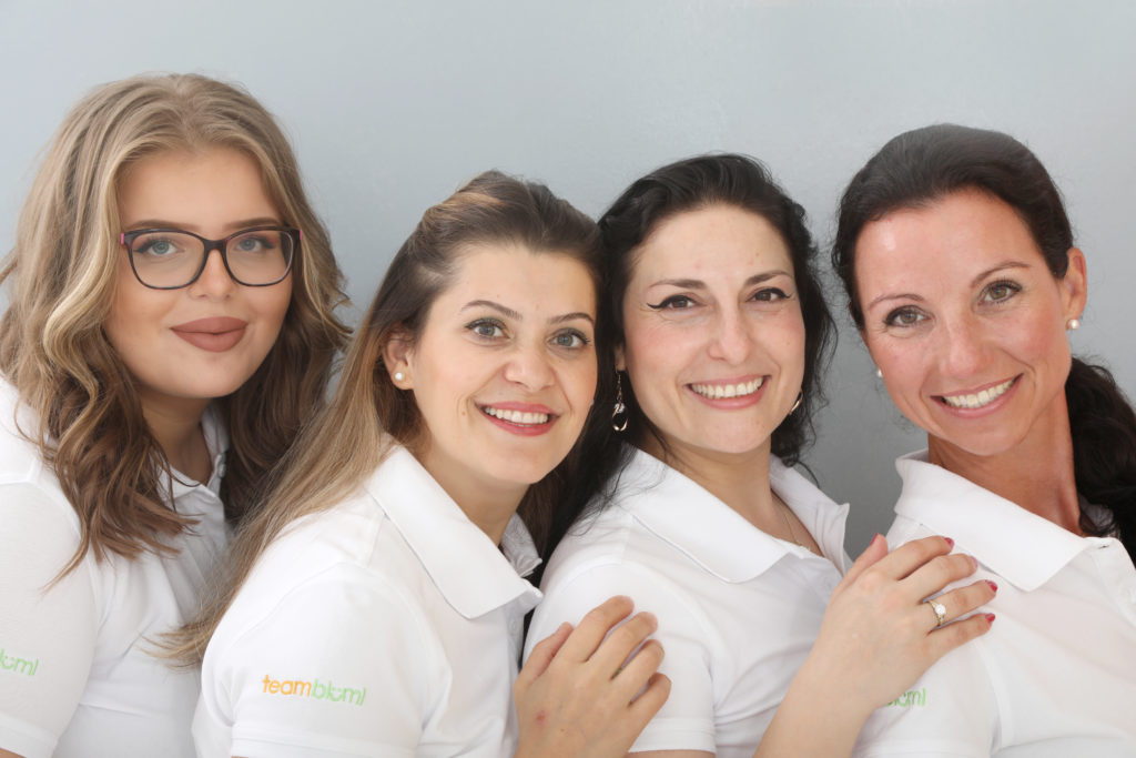 Vier lächelnde Frauen in weißen Polohemden mit dem Logo 'teambkm'