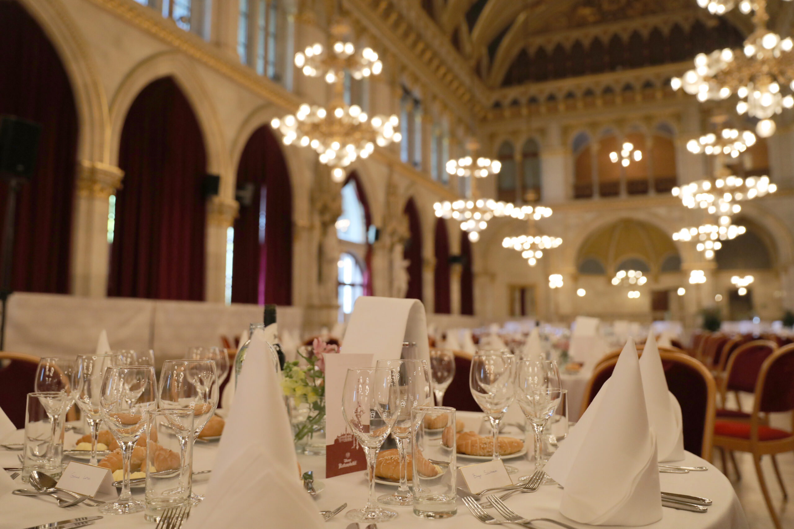 Festlich gedeckte Tische in einem eleganten Saal mit Kronleuchtern und historischer Architektur
