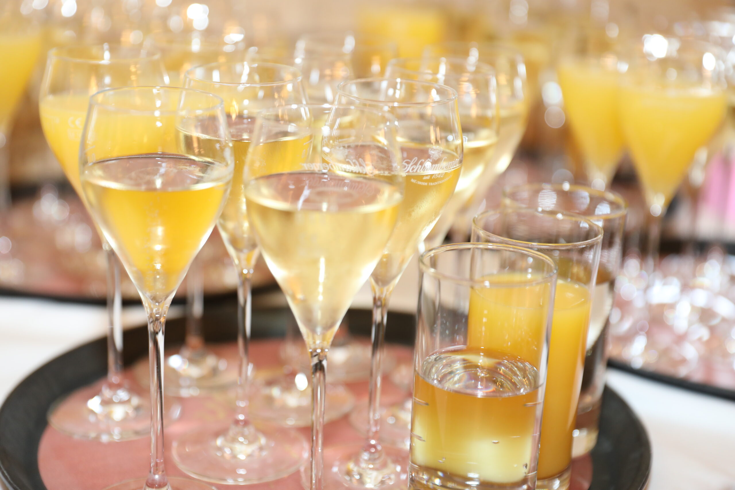Tisch mit Sektgläsern gefüllt mit gelblicher Flüssigkeit und Gläsern mit orangefarbenem Getränk