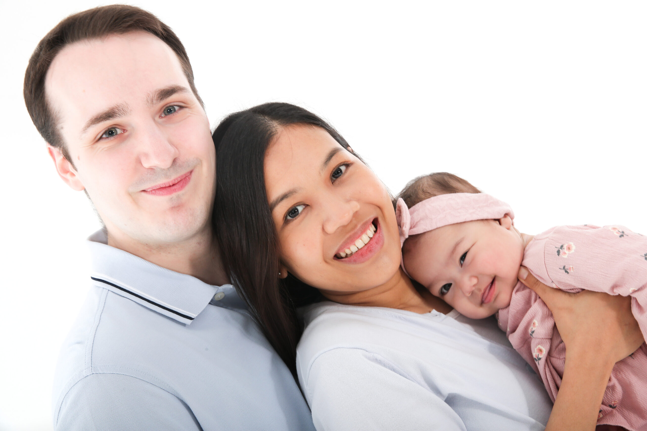 Eine glückliche Familie mit einem Baby lächelnd vor einem weißen Hintergrund.