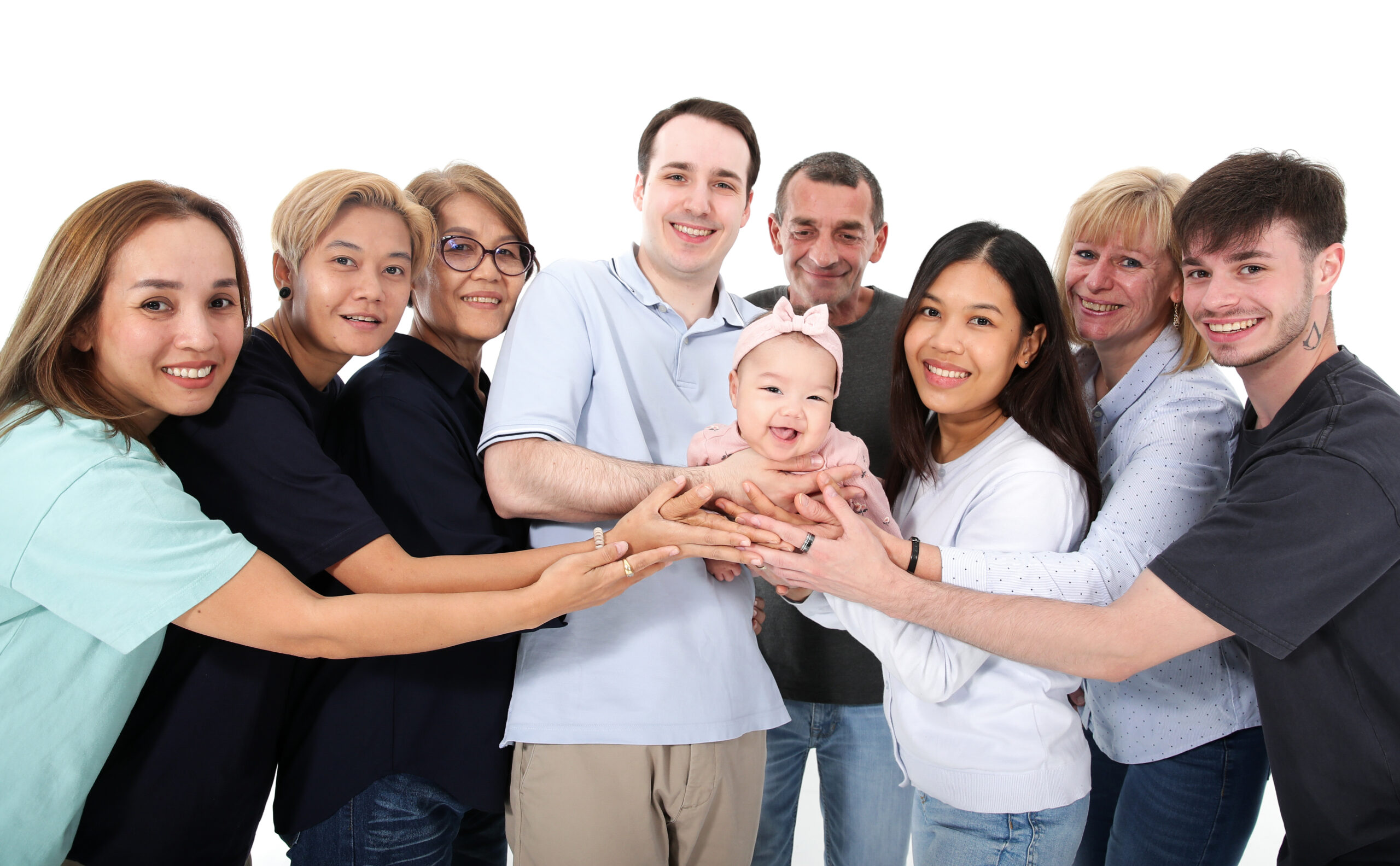 Glückliche, mehrere Generationen umfassende Familie lächelt in die Kamera, während sie ein Baby gemeinschaftlich halten.