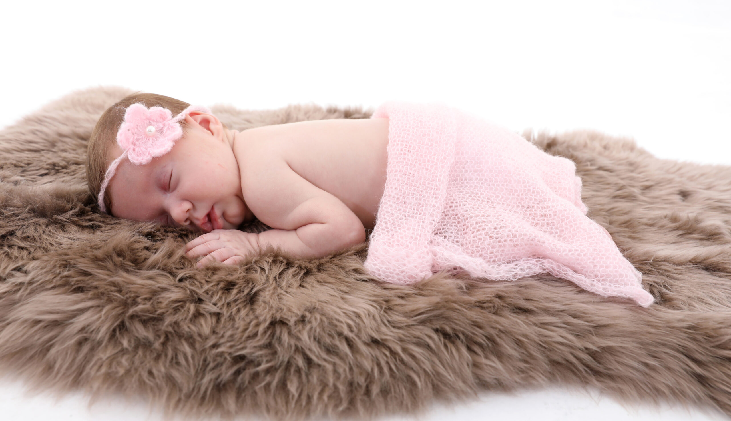 Schlafendes Baby mit rosa Kopfschmuck auf einer flauschigen Decke