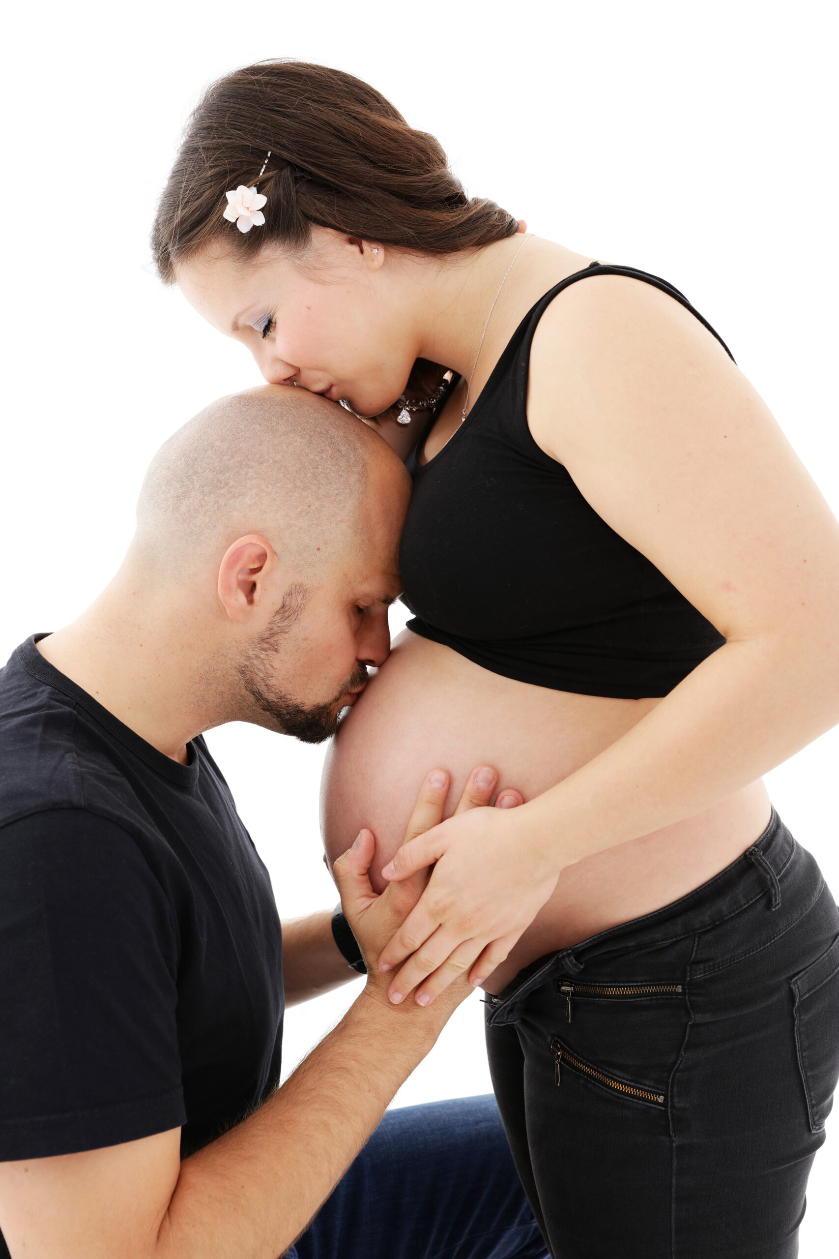 Zukünftige Eltern in liebevoller Umarmung, Mann küsst den schwangeren Bauch der Frau.