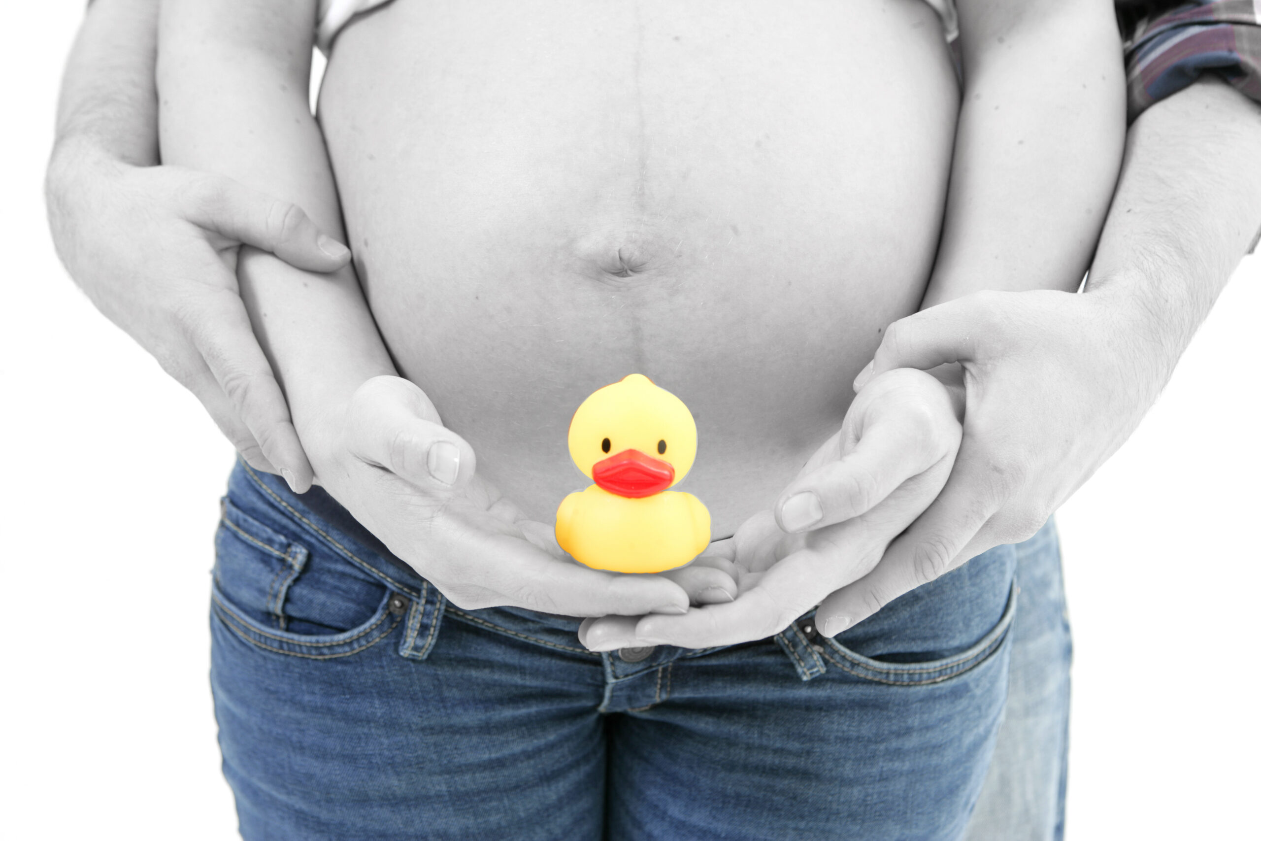 Schwangere Person mit entblößtem Bauch hält eine gelbe Gummiente, vor einem weißen Hintergrund